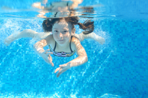 Young girl swimming underwater in blue pool