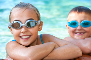 Two smiling children in pool wearing goggles